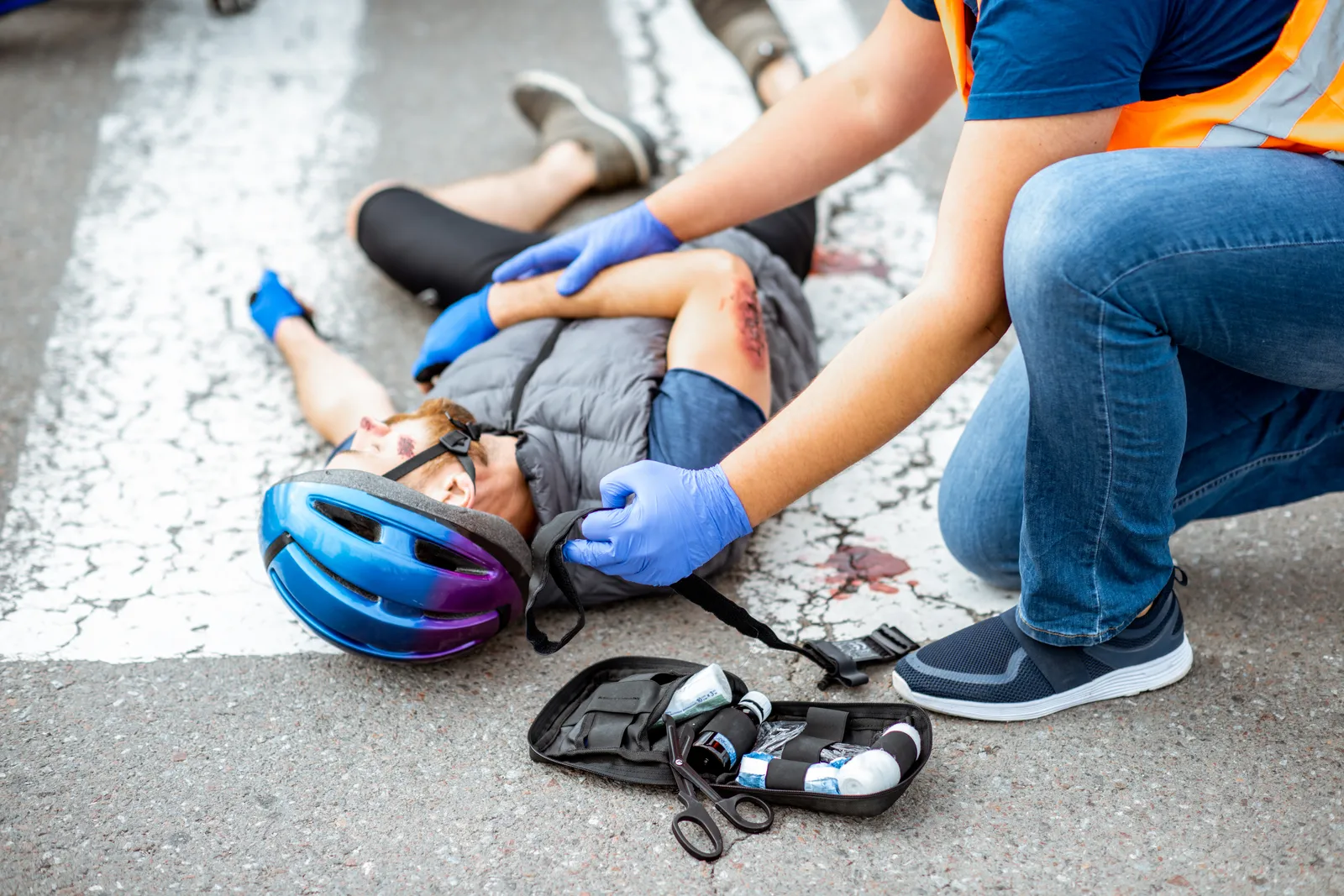 First responder helping an injured cyclist lying on the road beside his helmet