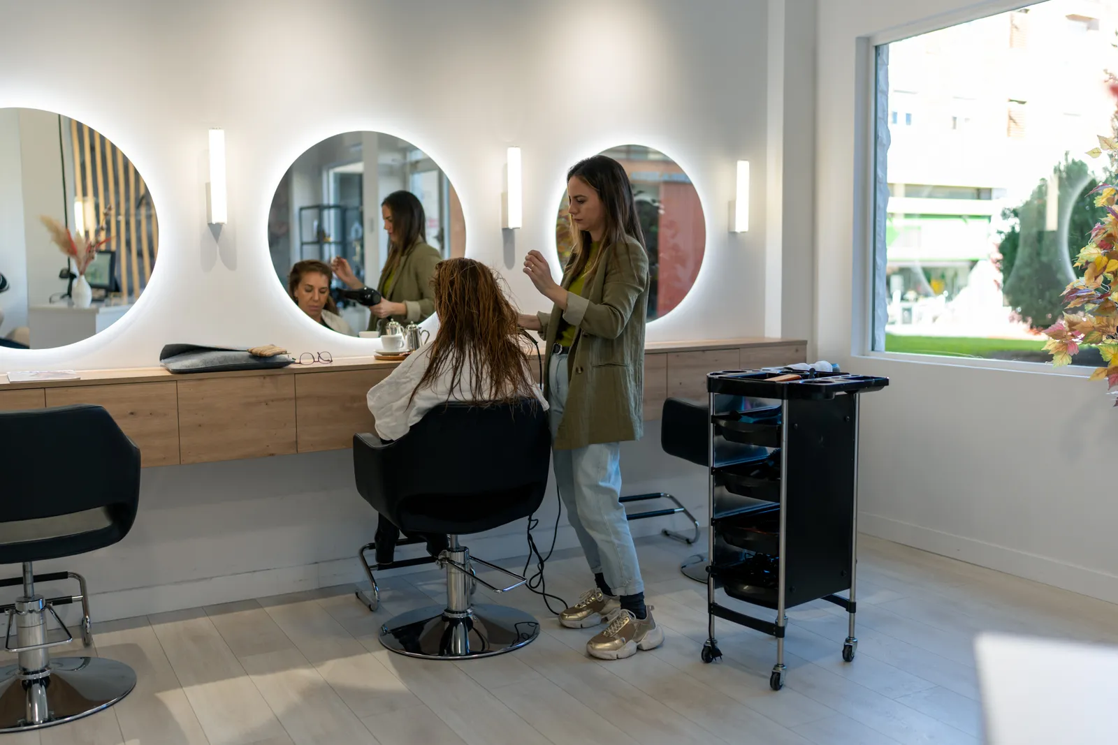 Stylist round-brushing a client's hair at a bright, mirrored blowout bar styling station