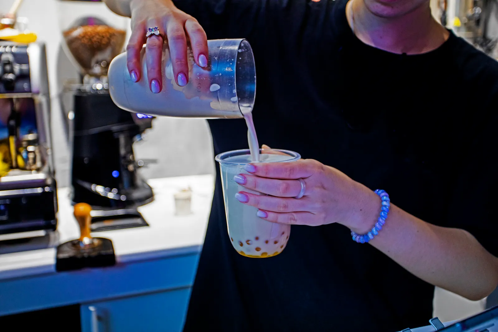 Barista shaking a fresh-made bubble tea with tapioca pearls behind the counter of a busy boba shop