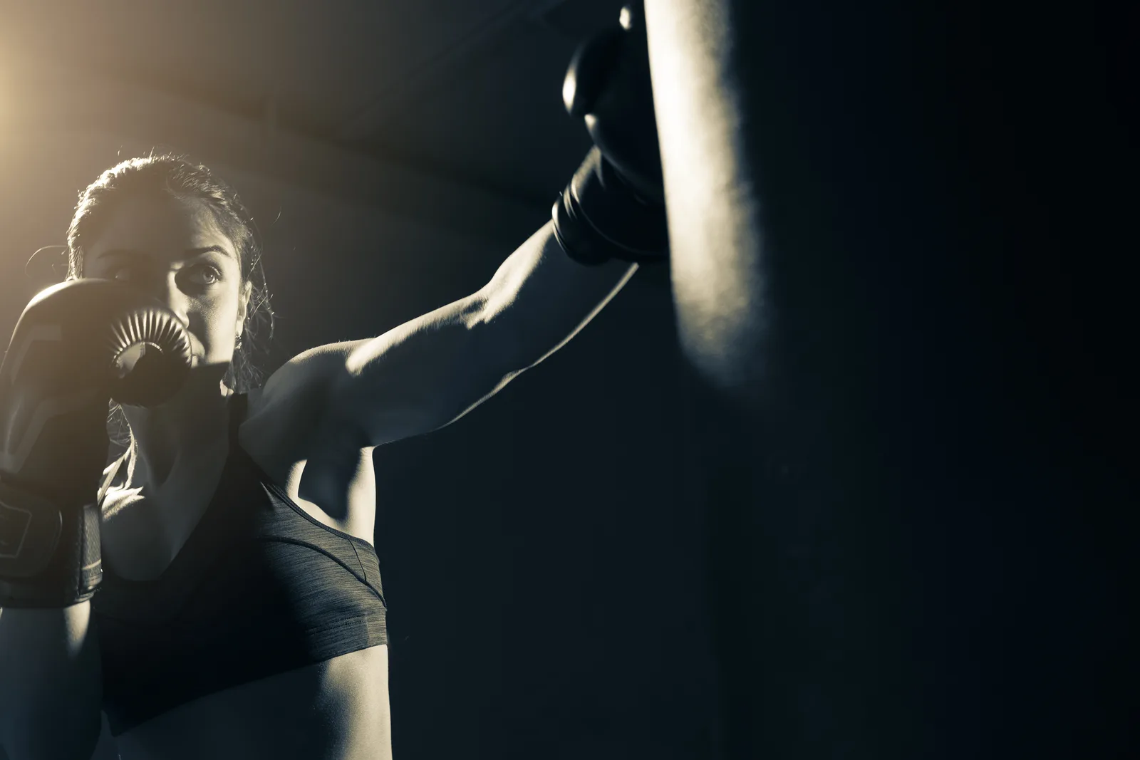 Boxing coach holding focus mitts for a member throwing a punch during a class at a boxing gym