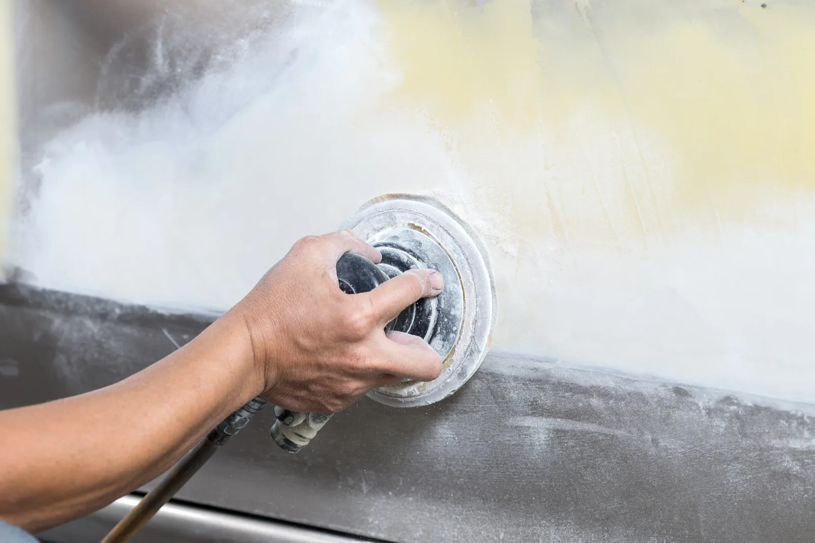 Restorer's hands wet-sanding a freshly painted vintage car body panel in a restoration shop