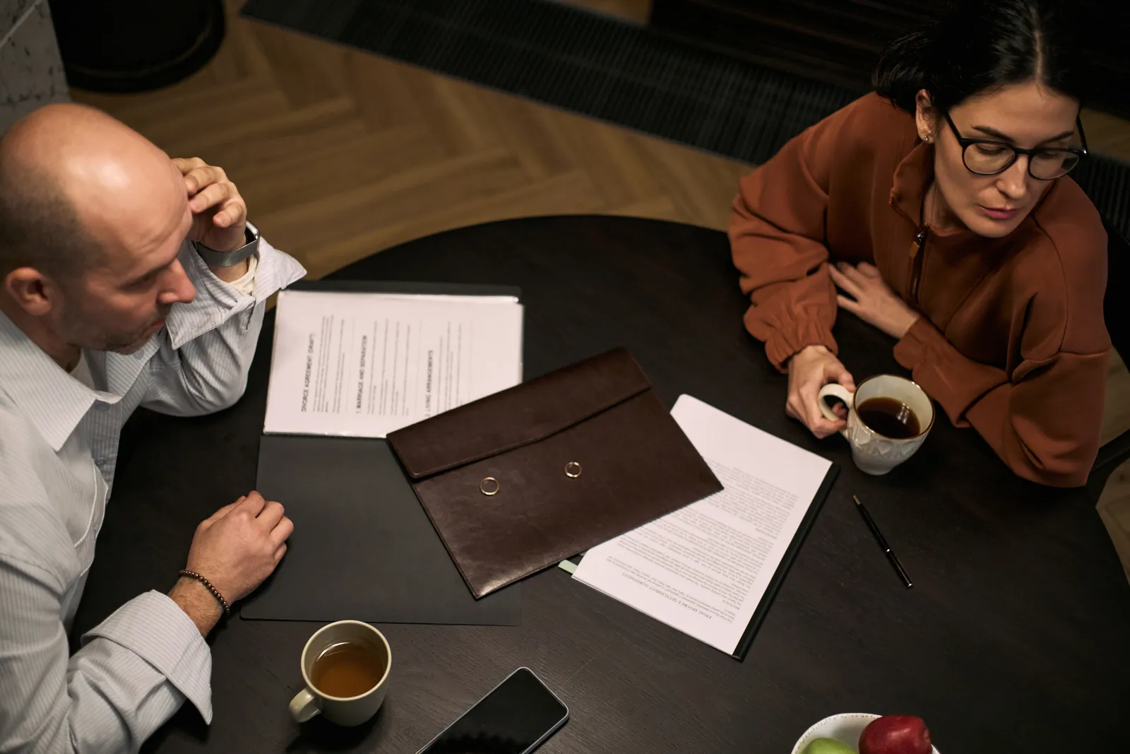 Clergy abuse attorney reviewing case documents with a client at a private conference table, a box of tissues and legal pad set between them