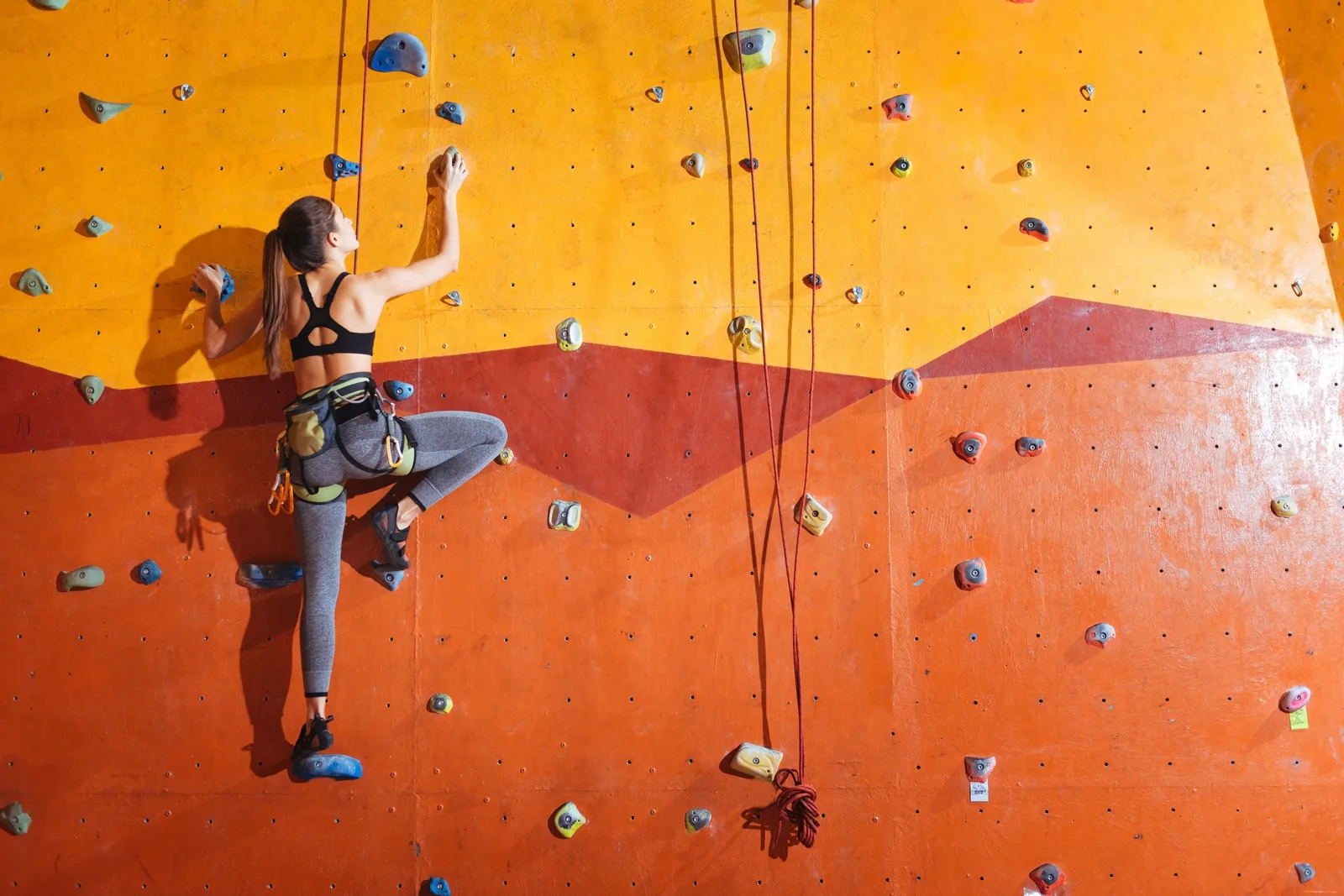 Climber reaching for a hold on a colorful bouldering wall inside an indoor climbing gym