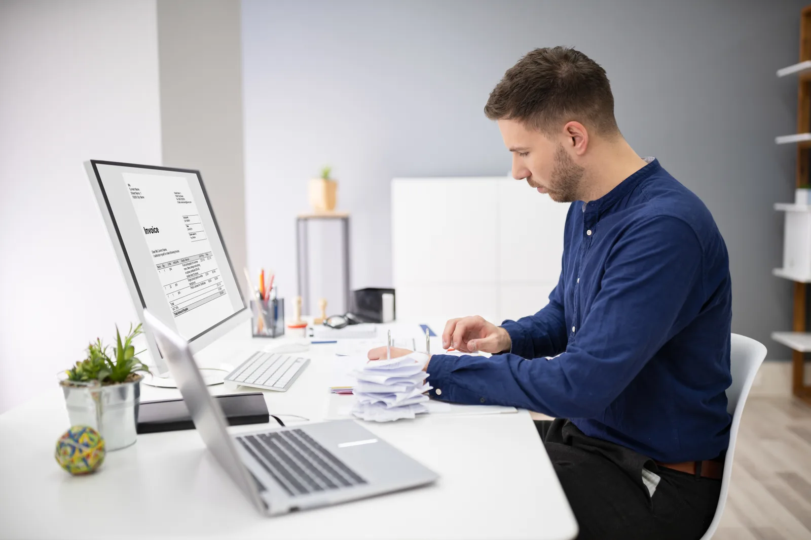 Commercial collections specialist reviewing past-due business invoices and account files at a desk
