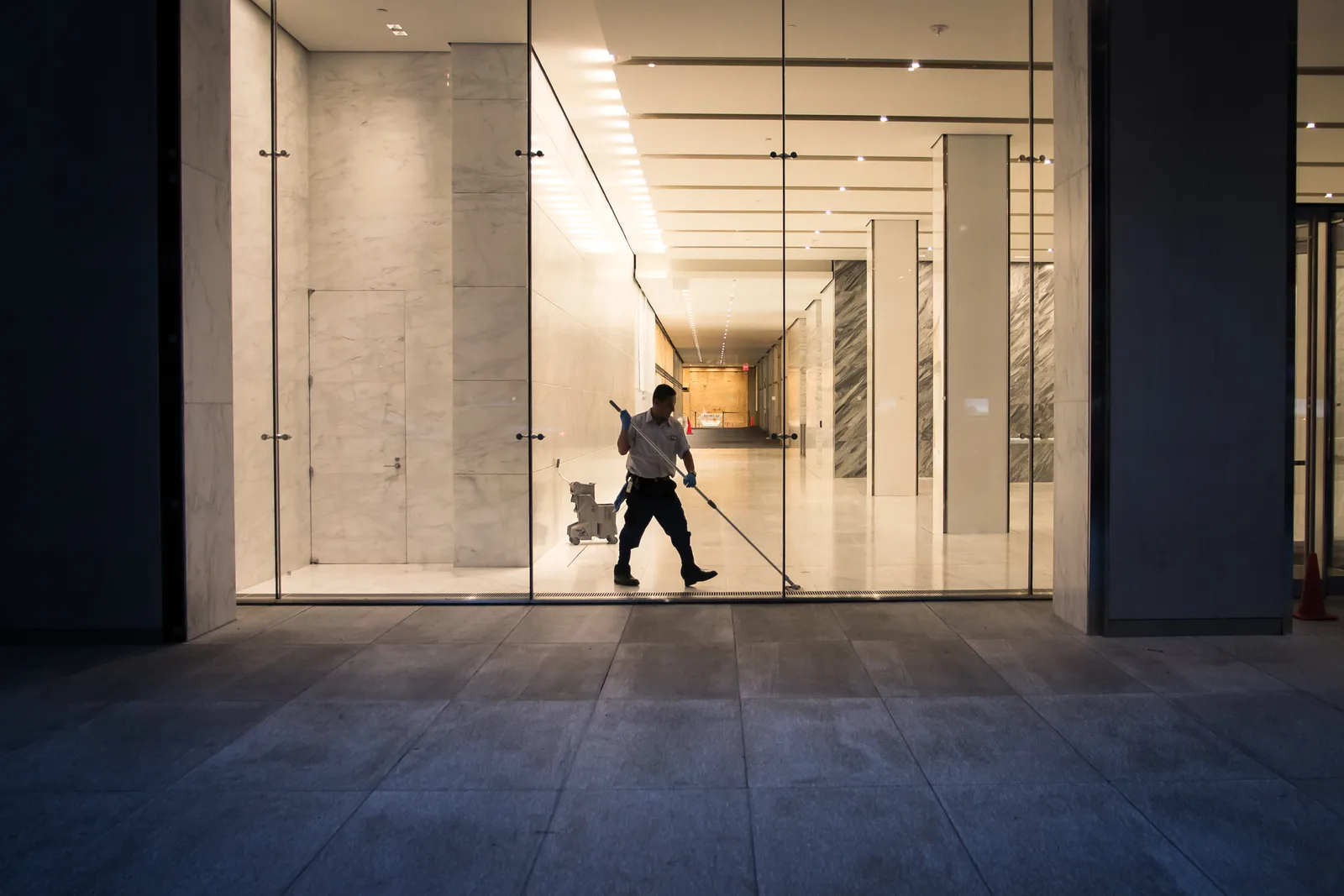 Commercial cleaner in uniform polishing the floor of an office building lobby after hours