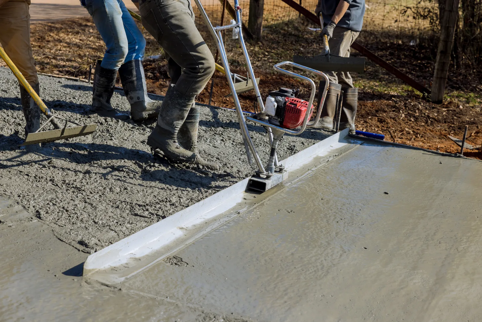 Concrete crew screeding a freshly poured driveway slab while a finisher smooths the edge