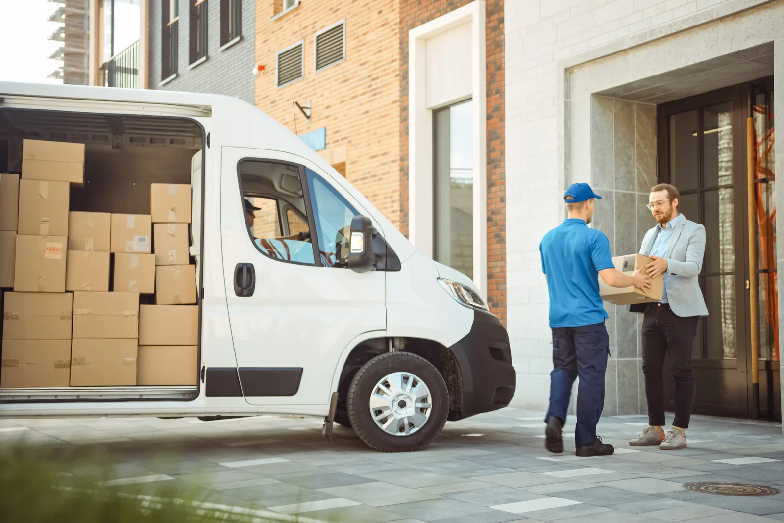 Courier in a delivery vest carrying a package from his van to a customer's door