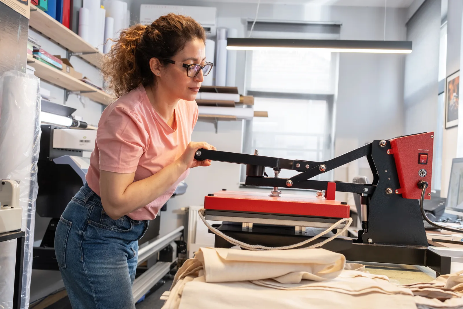 A screen printer pulling ink across a screen onto a t-shirt on a press in a custom apparel shop