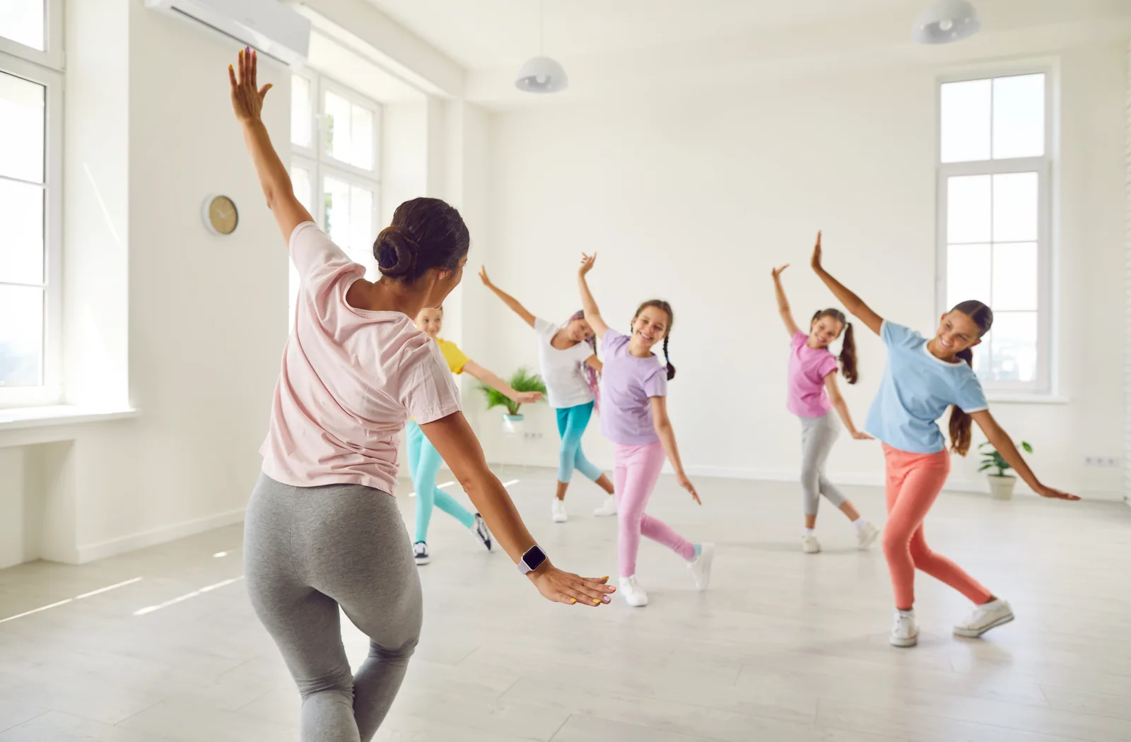 A dance teacher demonstrating steps as young students follow her routine on the studio floor