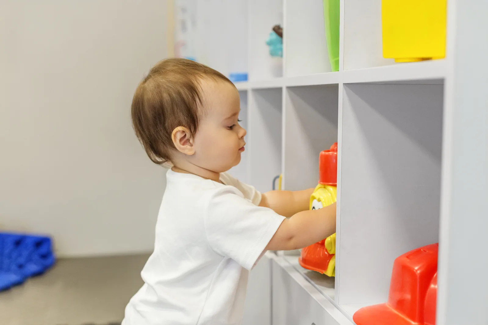 A daycare teacher helping toddlers with a group activity at a table in a bright, full-day child care classroom