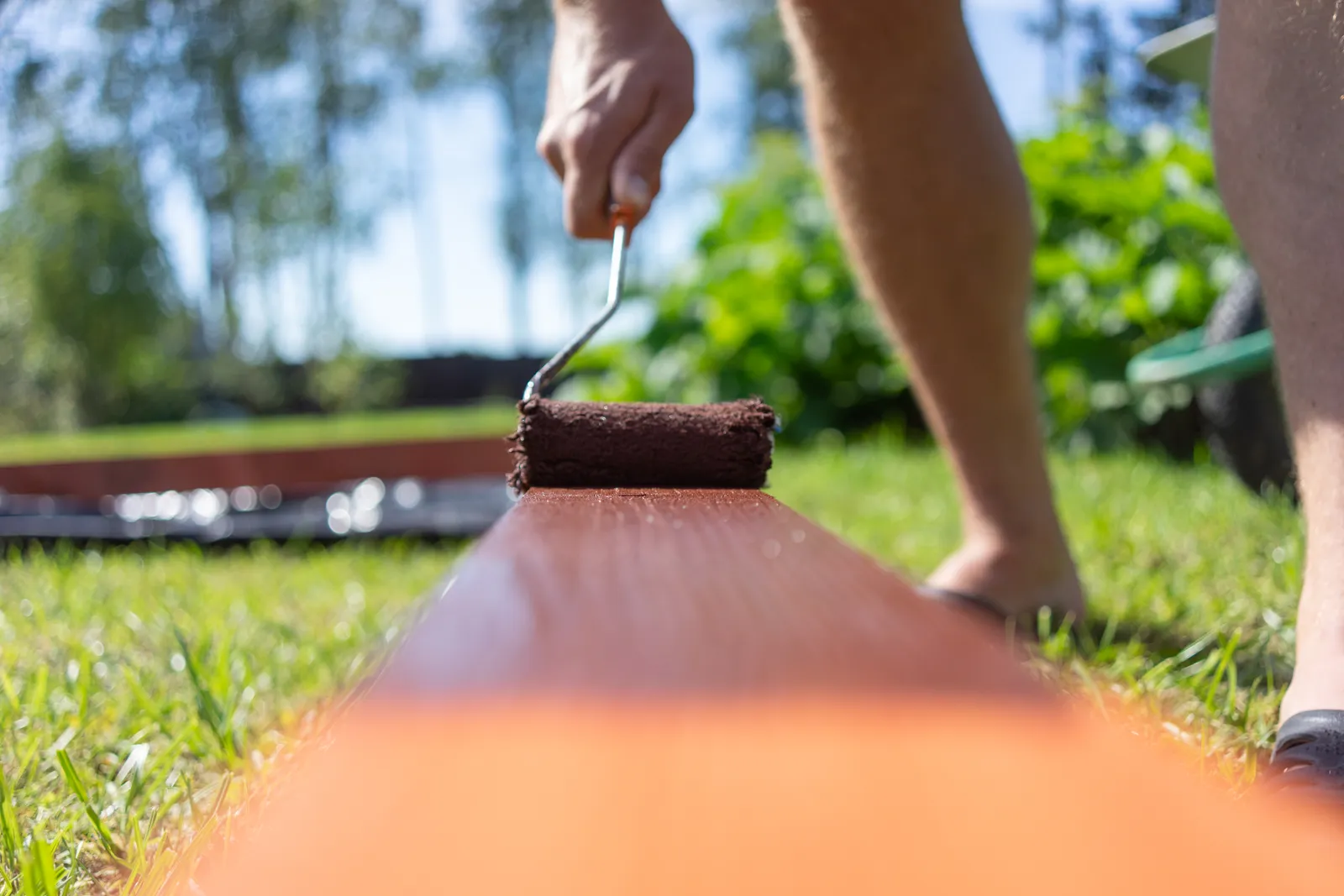 Contractor rolling fresh stain onto a freshly sanded backyard deck after pressure washing