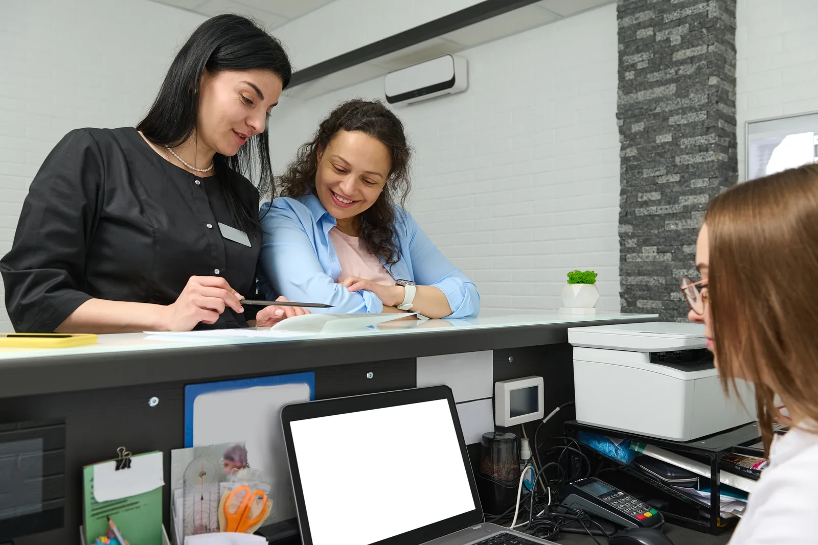 Software team reviewing a patient scheduling and treatment-plan dashboard together at a laptop in their office
