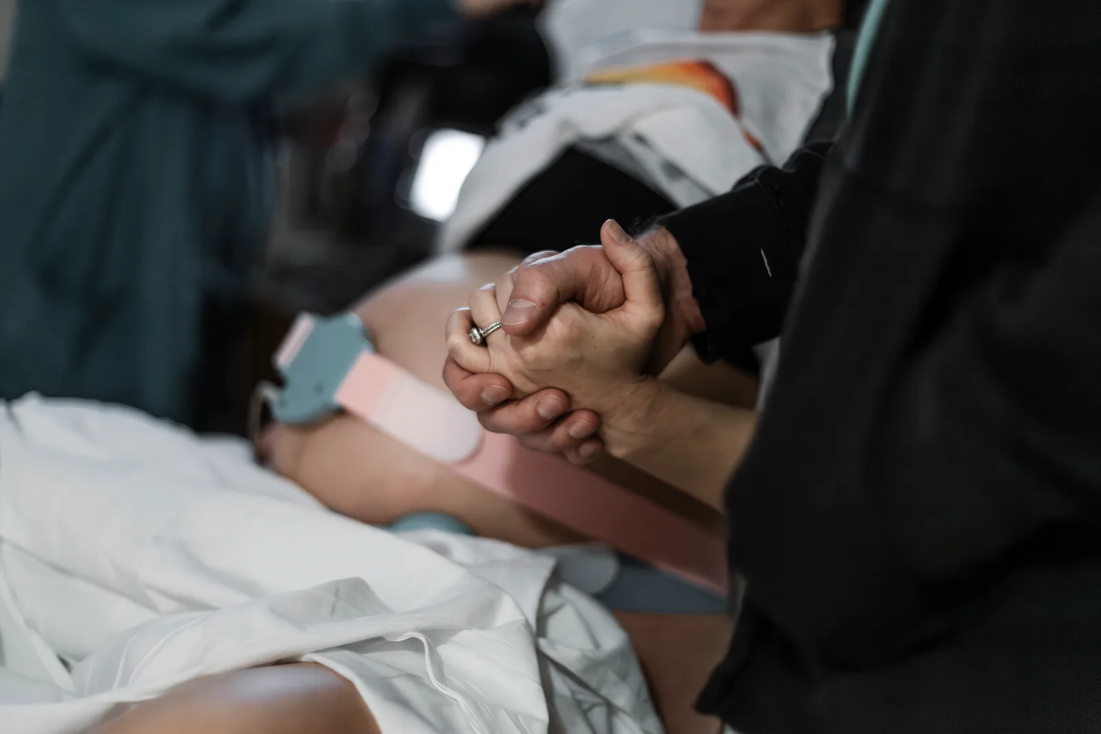 A birth doula holding a laboring mother's hand and offering quiet comfort during labor in a birth room