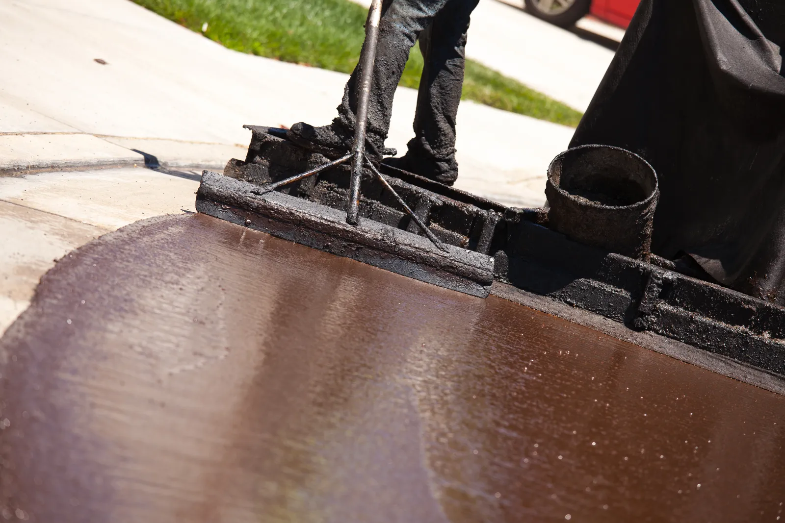 Worker using a long-handled squeegee to spread fresh black sealcoat across a residential asphalt driveway