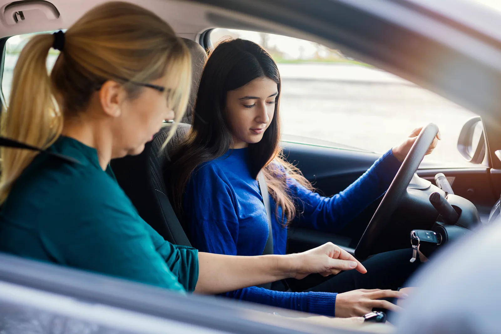 Driving instructor in the passenger seat coaching a teen student behind the wheel during a lesson
