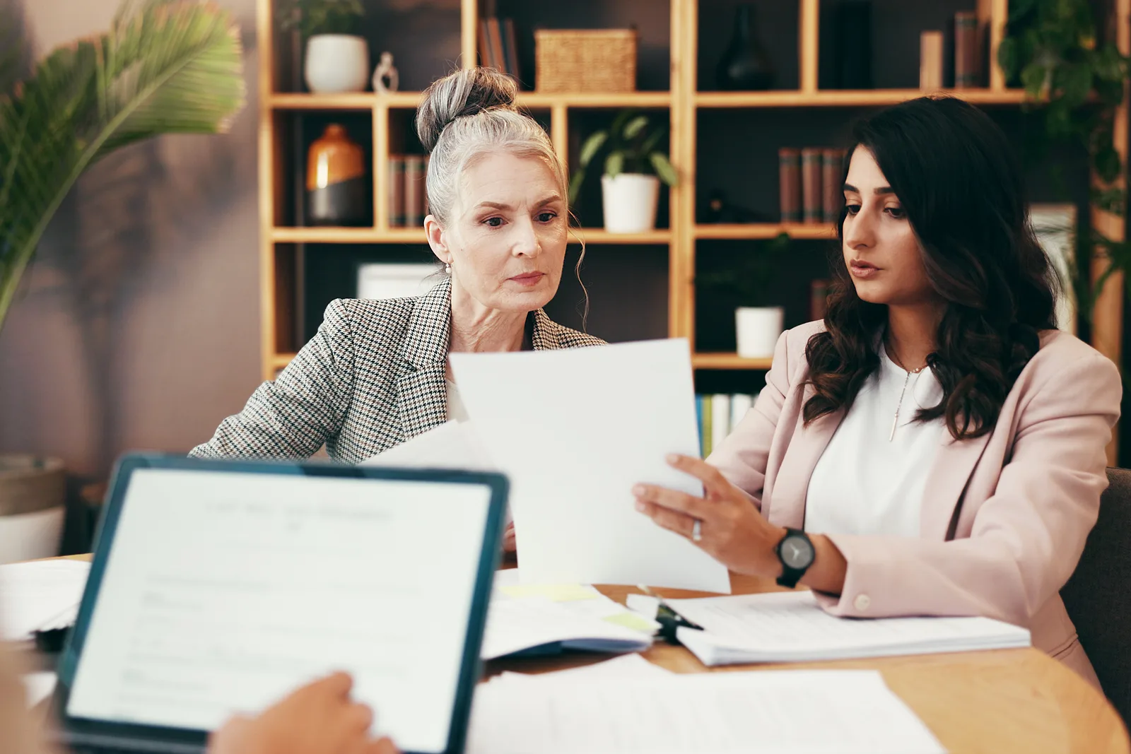 Elder law attorney sitting with an older client and her adult daughter, reviewing Medicaid and long-term-care planning documents at a desk