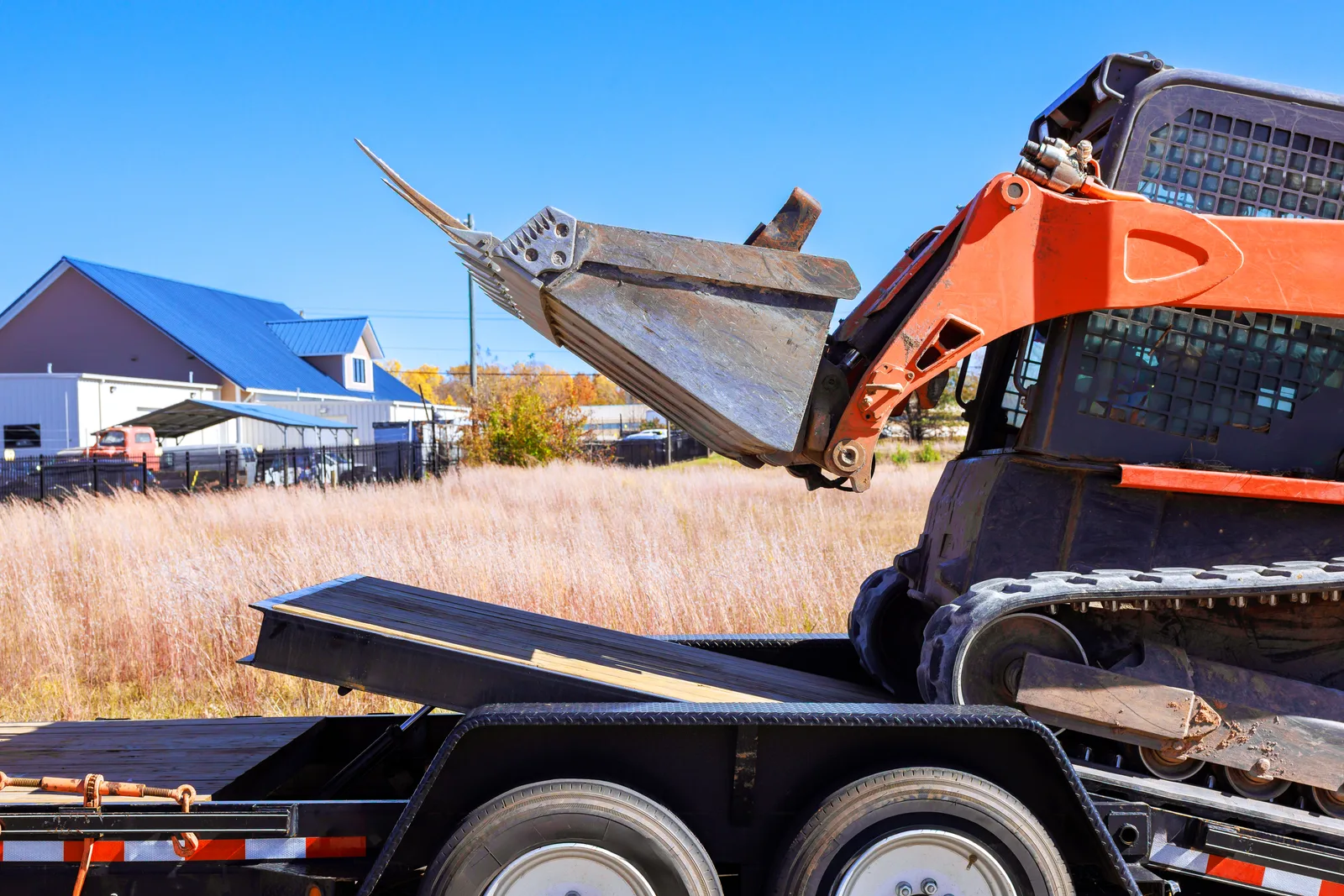 Rental yard worker loading a skid steer onto a flatbed trailer for delivery to a job site