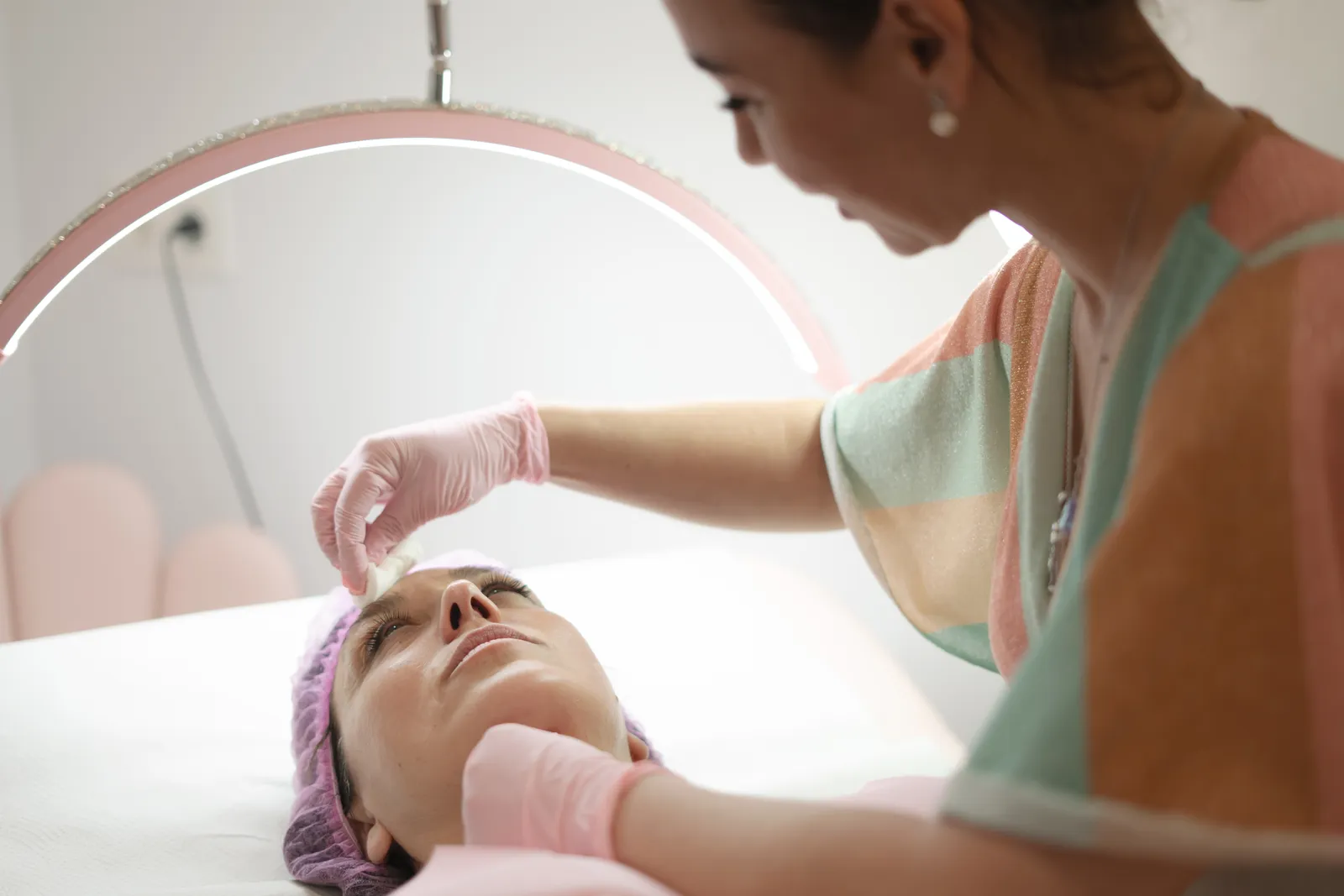 Esthetician applying a facial mask to a client's skin at a treatment bed in a calm, clean studio