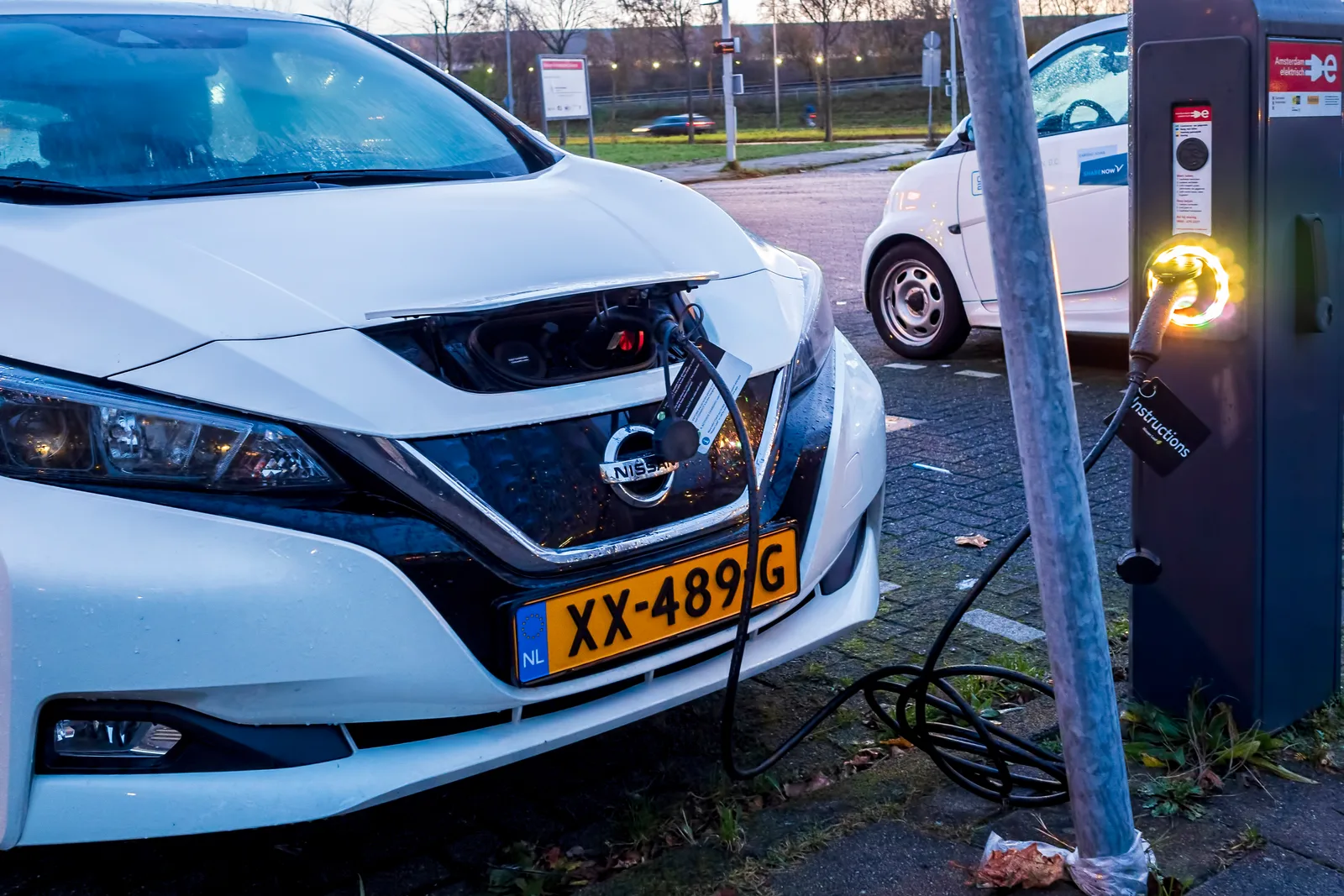 Certified electrician installing a Level 2 EV charger on a garage wall next to a parked electric vehicle