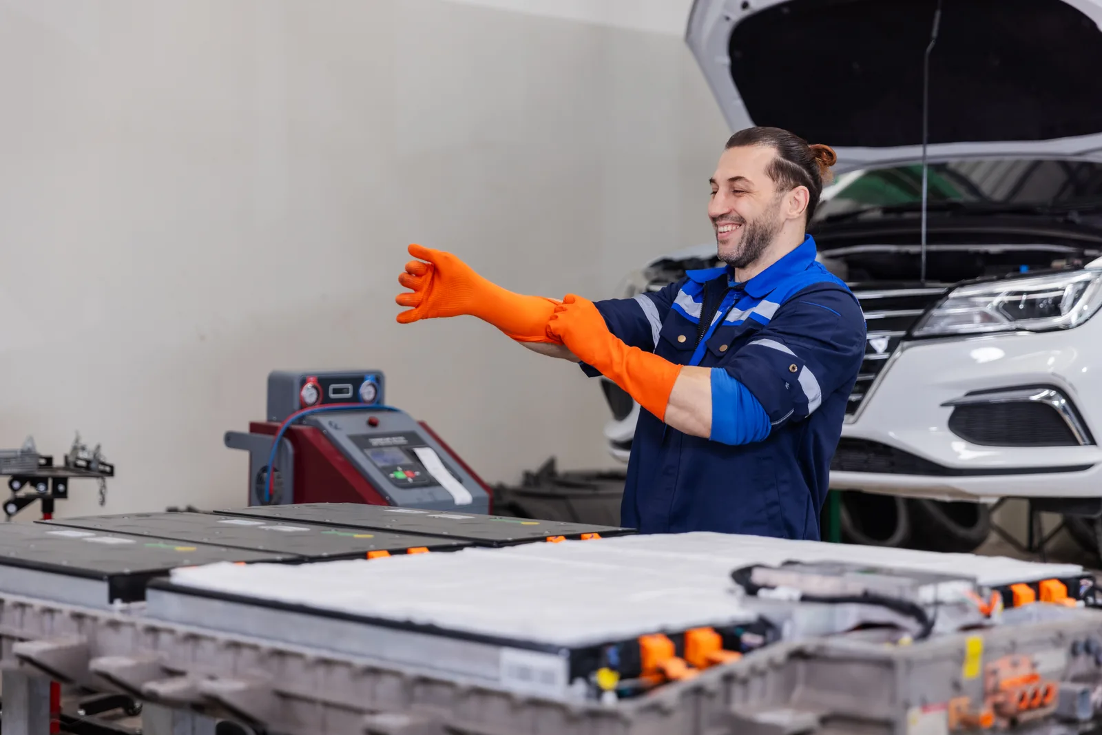 Technician in insulated high-voltage gloves working on an electric vehicle's battery pack in a repair shop bay