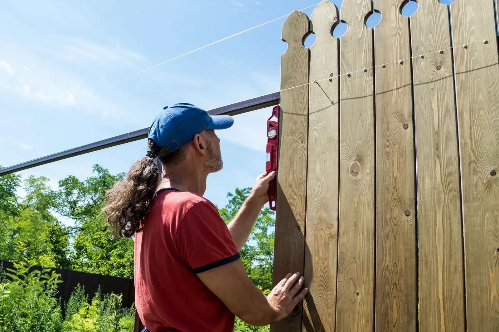 Fence installer leveling a wood privacy panel between set posts in a homeowner's backyard