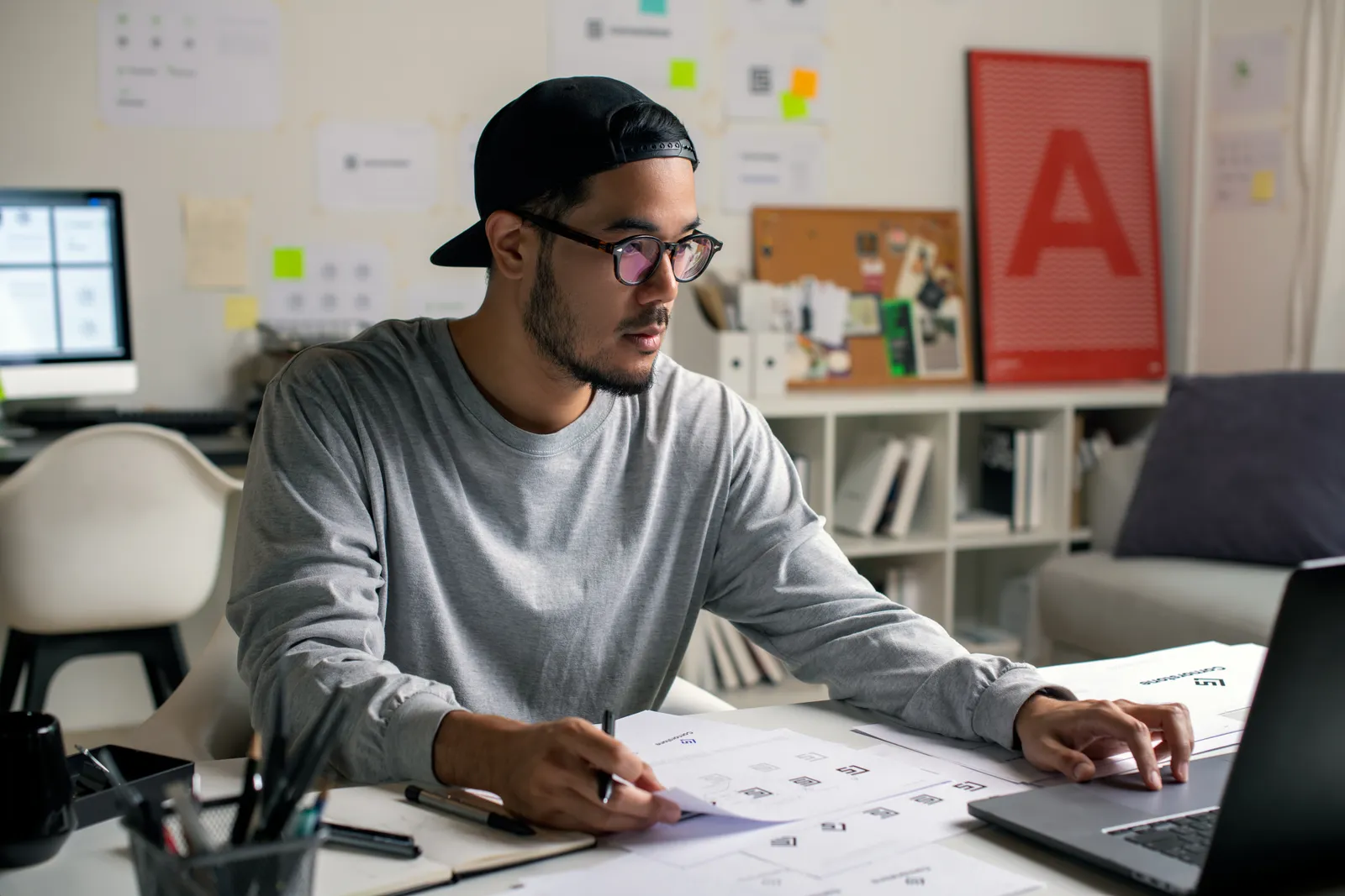 Independent type designer reviewing a typeface specimen sheet and weight chart on a laptop at a studio desk