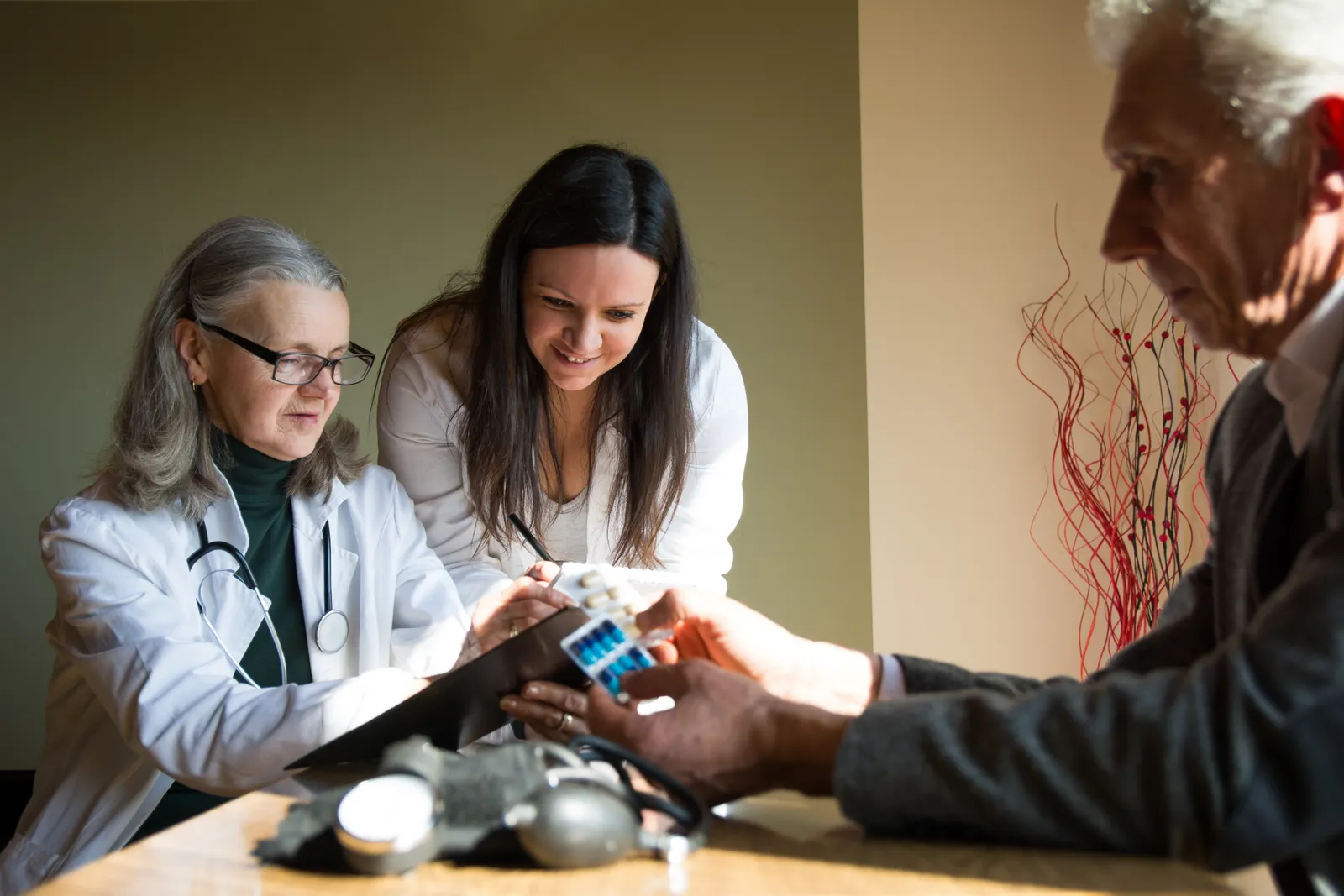 Geriatrician reviewing a medication list with an older patient and her adult daughter during an office visit