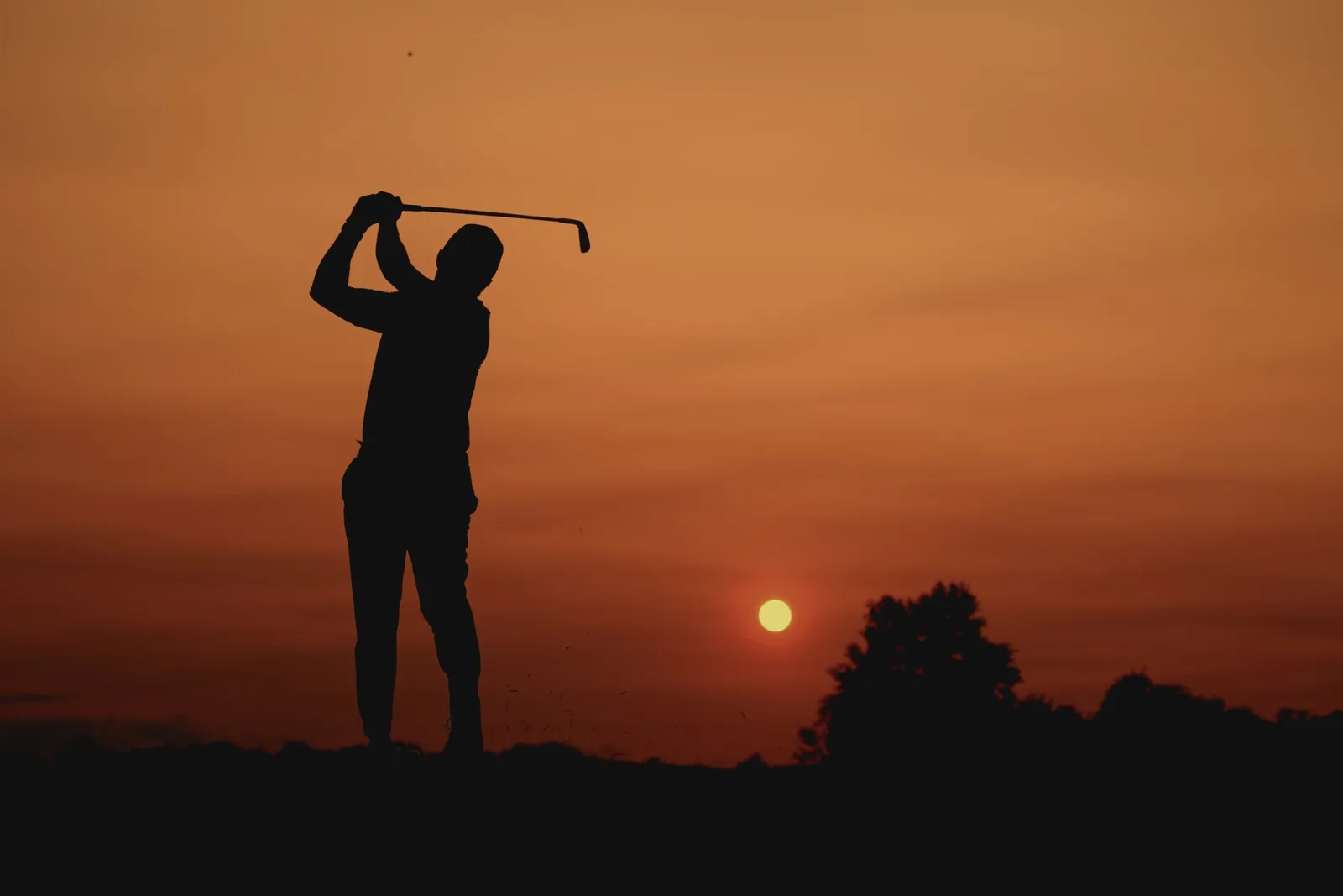 Golfer teeing off at golden hour on a lush green fairway lined with trees