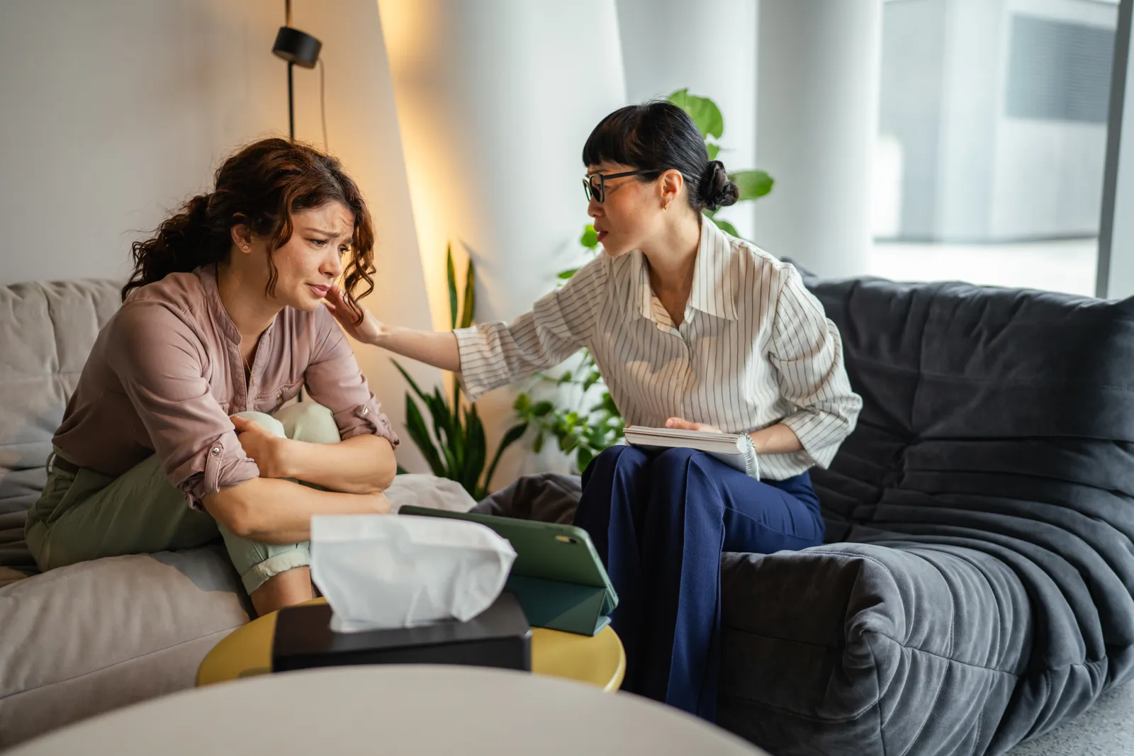 Grief counselor sitting across from a client in a warm, softly lit therapy office during a one-on-one session