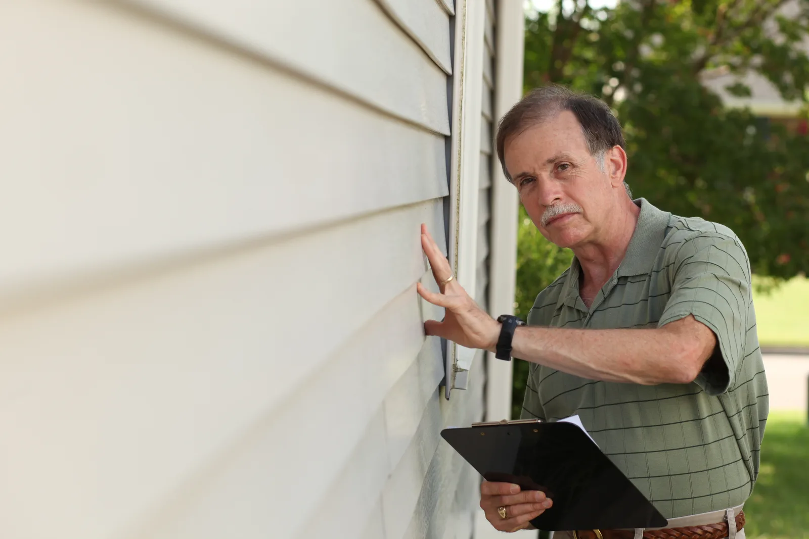 Home inspector noting roof and siding findings outside a house that is under contract