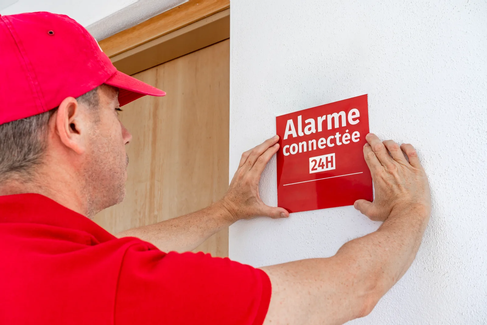 Technician mounting a security camera under a home's eave while installing an alarm system