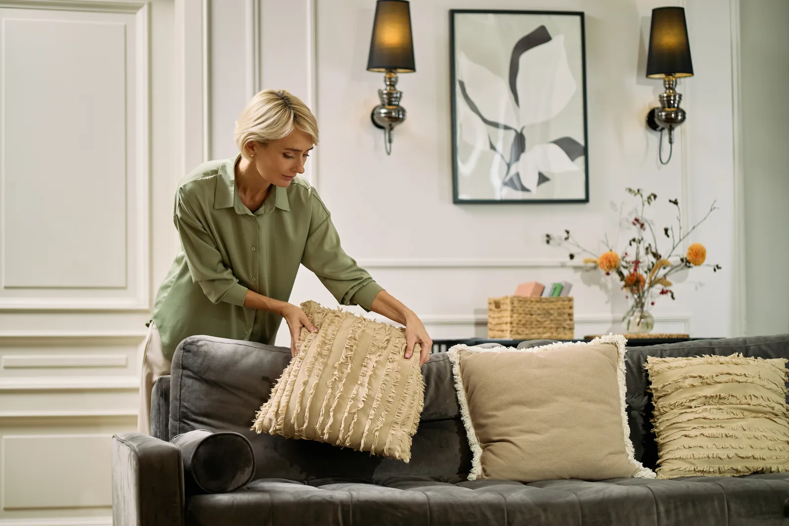 Home stager arranging throw pillows on a sofa in a bright, freshly staged living room before listing photos