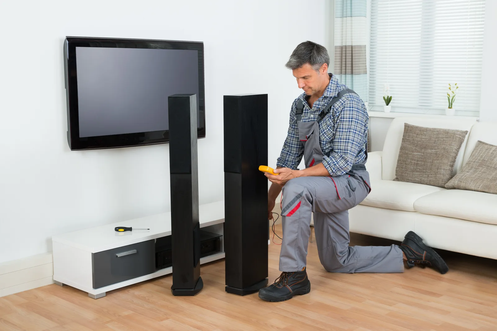 Installer mounting a large flat-screen TV in a custom home theater with tiered leather seating