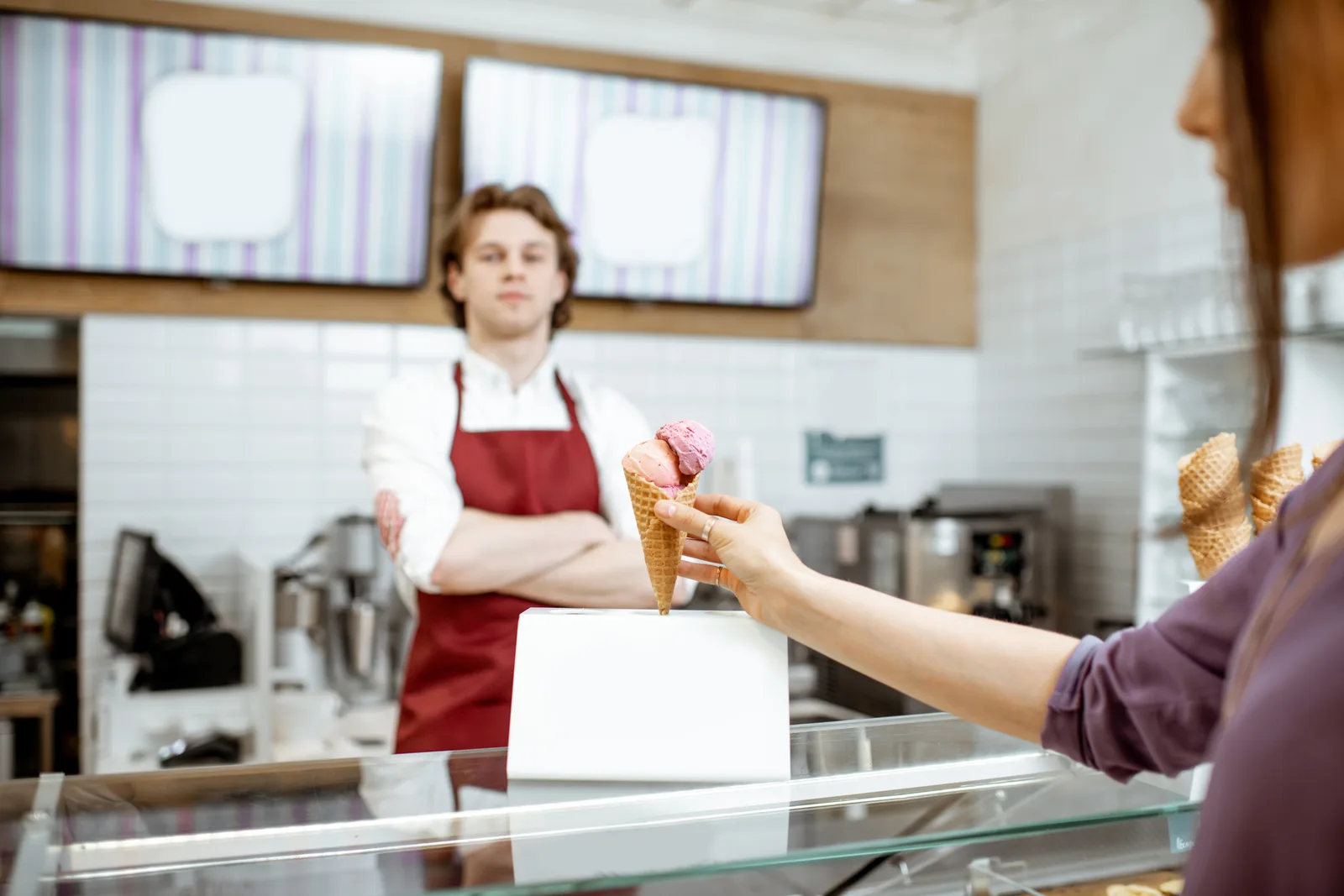Server handing a fresh ice cream cone across the counter to a customer at a busy scoop shop