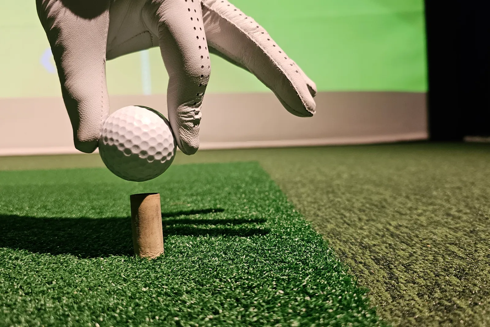 Teeing up a ball on the turf of an indoor golf simulator bay