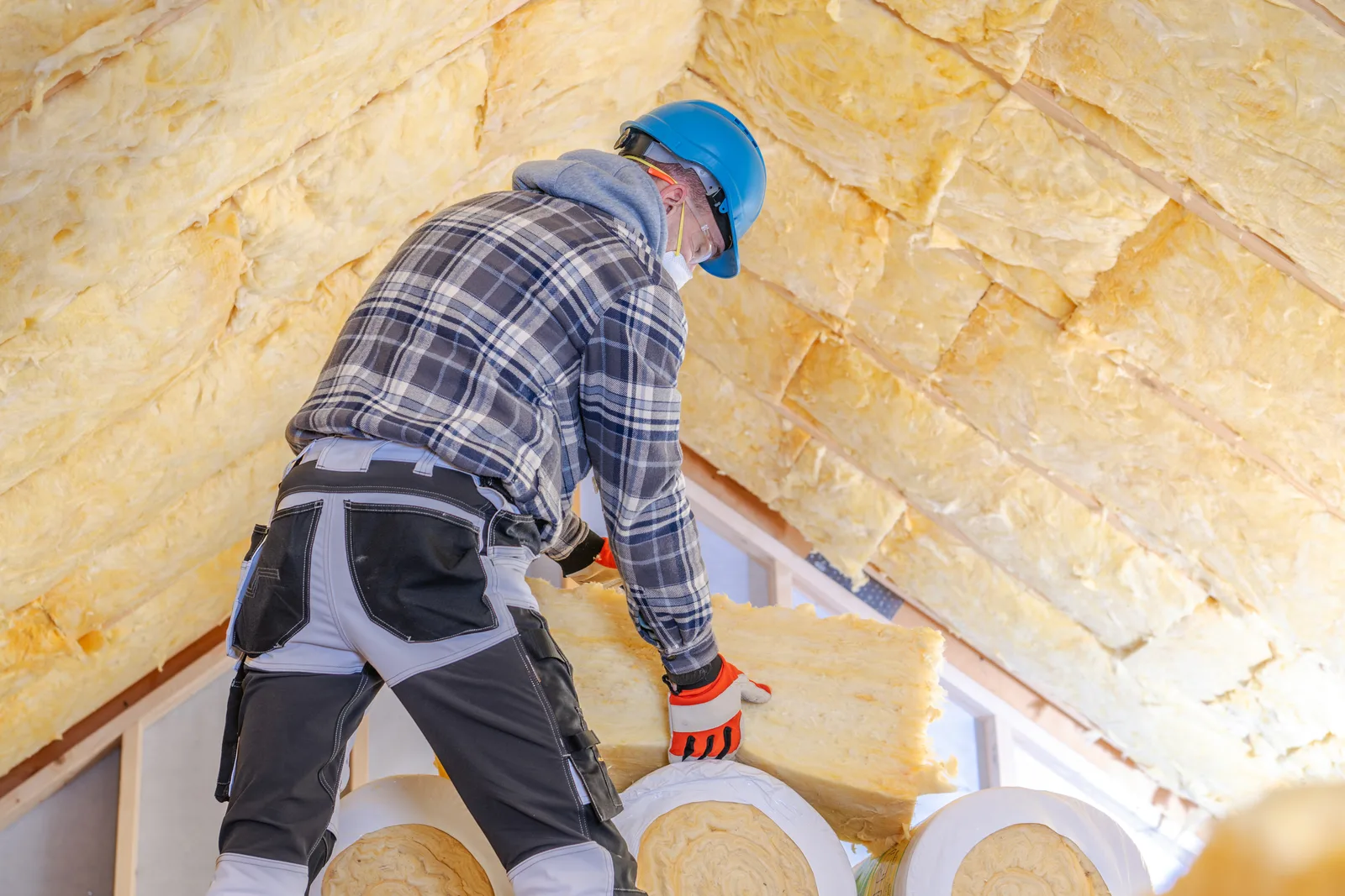 Insulation contractor in protective gear spreading blown-in insulation across an attic floor