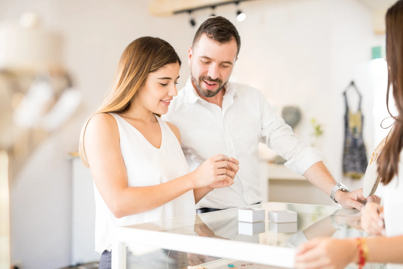 Jeweler helping a couple try on engagement rings at a lit display counter in a jewelry store