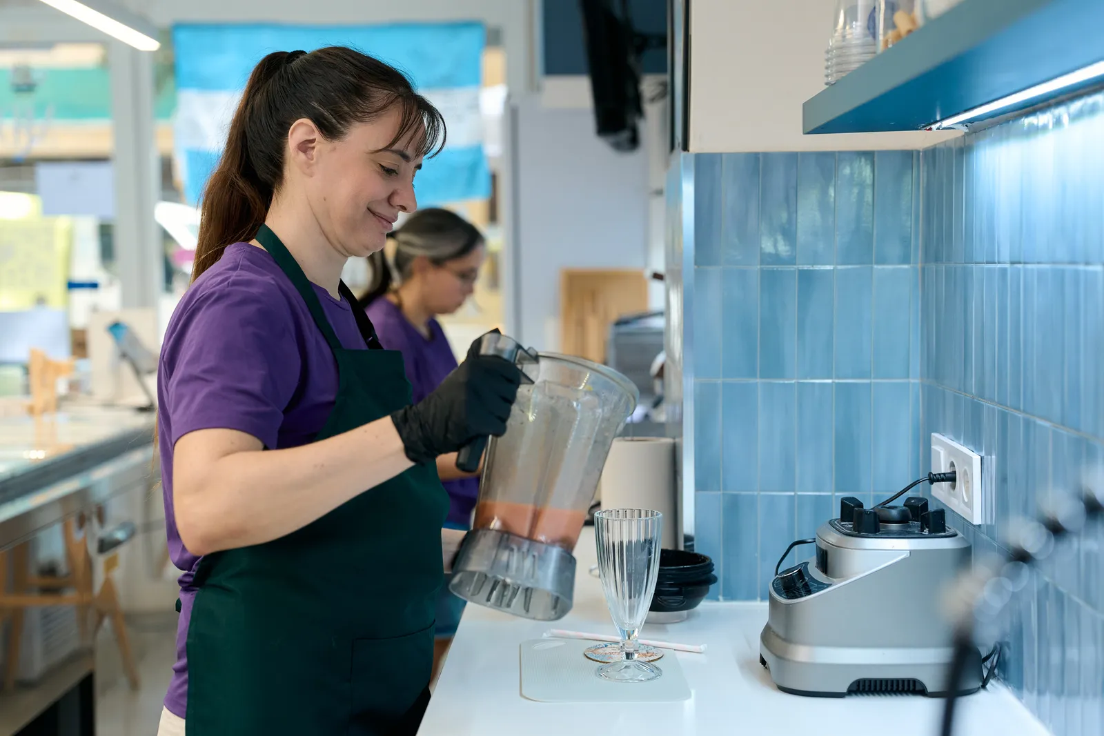 Employee blending a fresh fruit smoothie behind the counter of a busy juice and smoothie bar