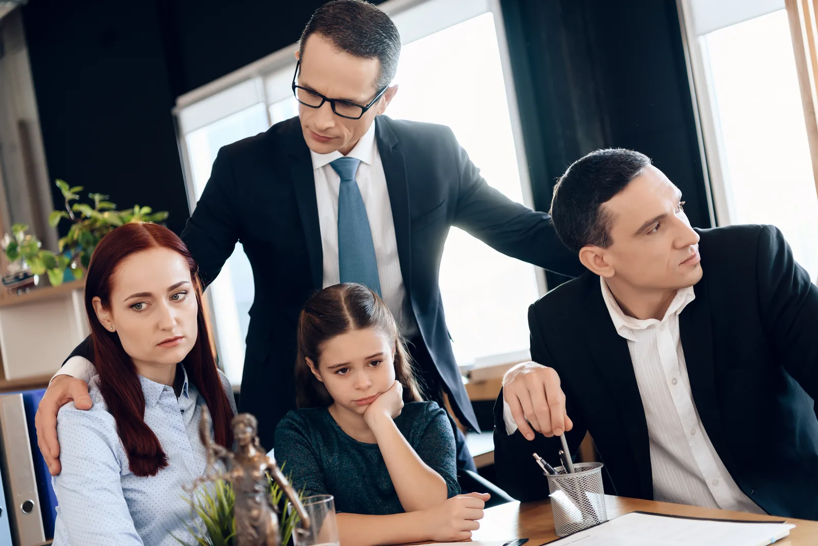 Juvenile defense attorney sitting with a teenage client and a parent, reviewing case paperwork together in a law office