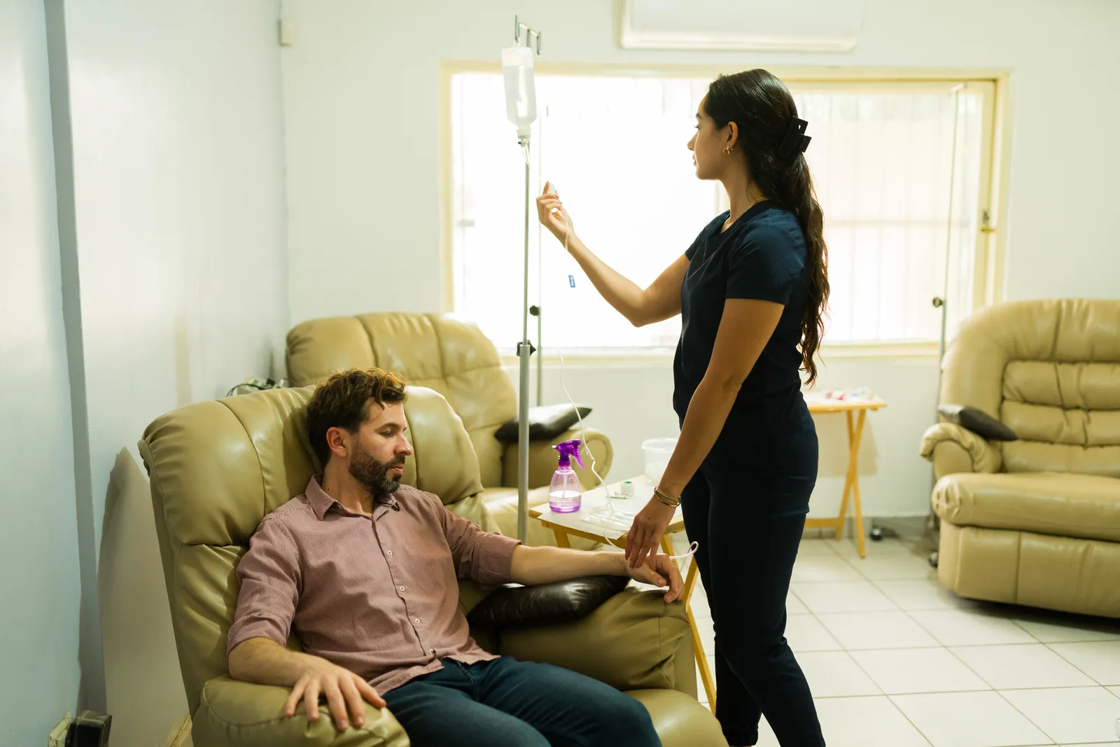 Patient reclining with an IV infusion while a clinician checks on him