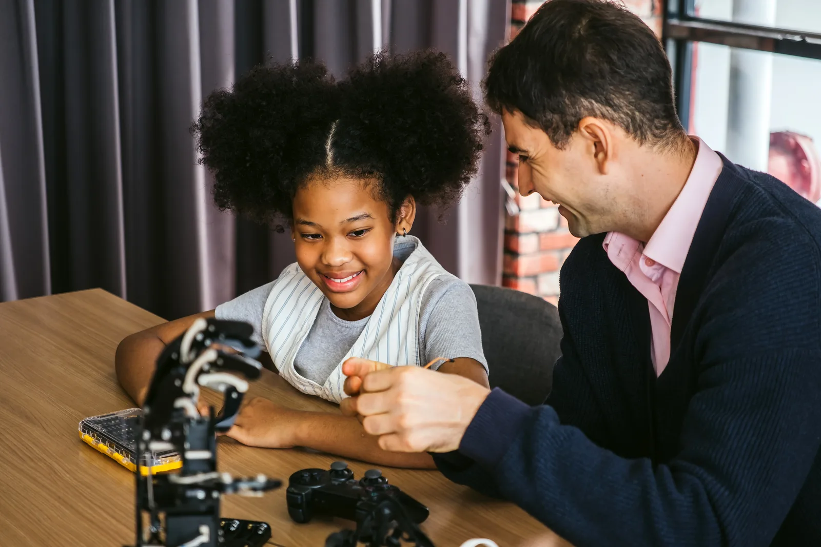 Instructor helping two elementary-age kids program a small robot on a laptop in a coding academy classroom