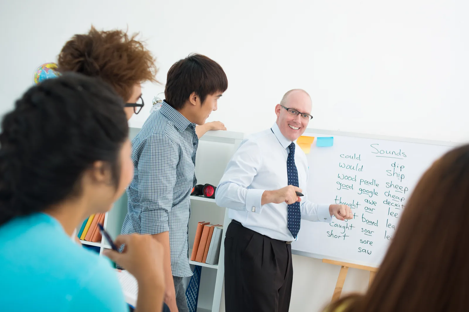 Language teacher leading a small adult class through a speaking exercise at a whiteboard