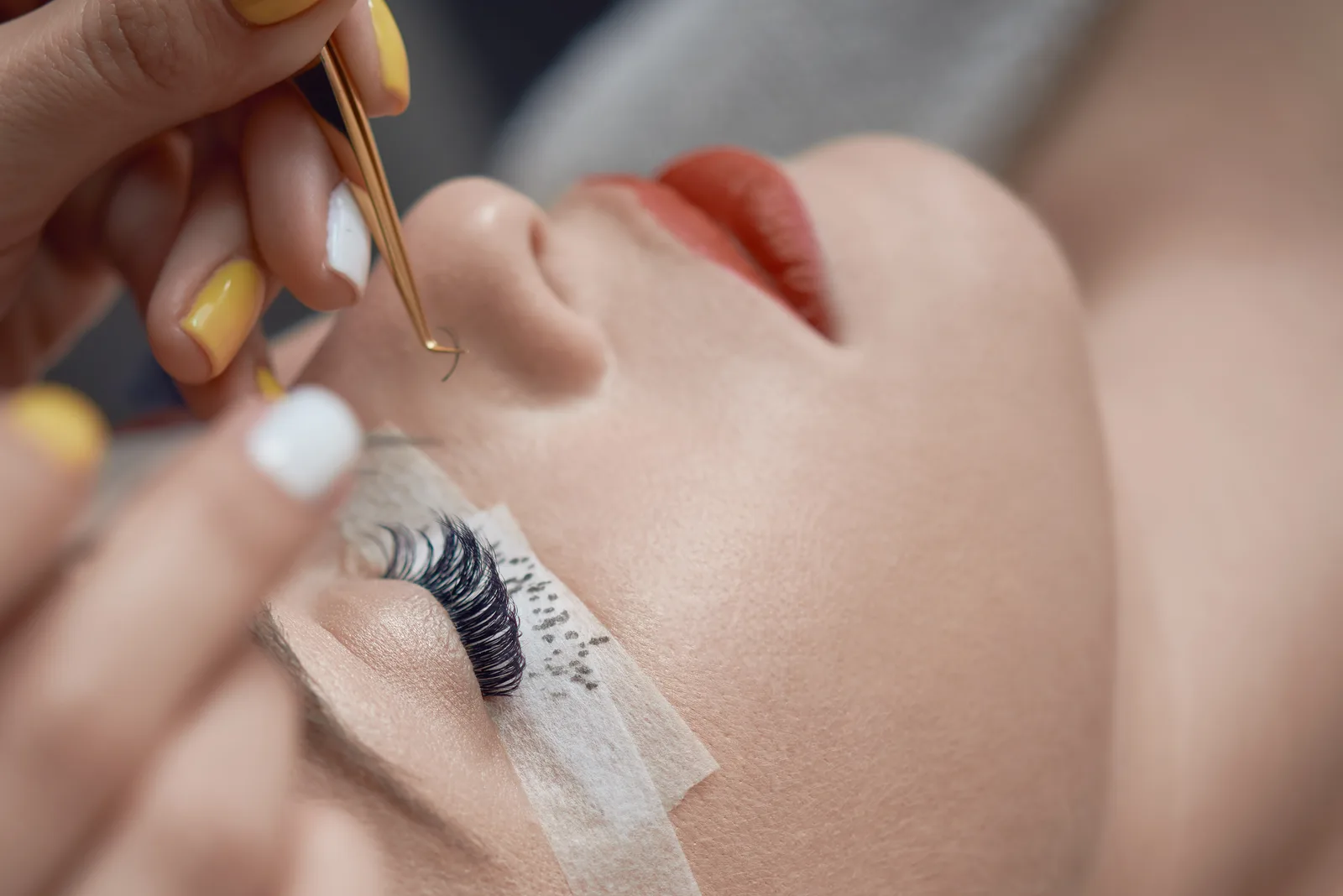 Lash artist applying individual eyelash extensions to a reclined client in a bright studio