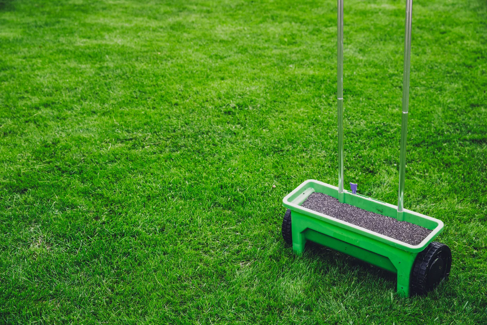 A lawn care technician mowing a striped lawn in a residential front yard with an equipment trailer parked at the curb