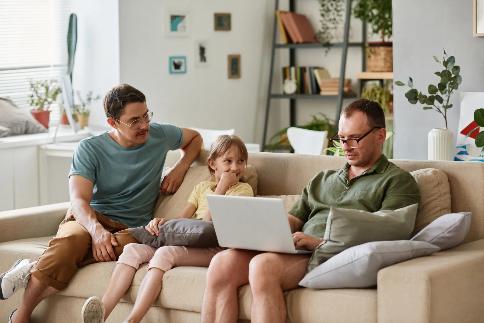 Two dads and their daughter looking at a laptop together on the family couch