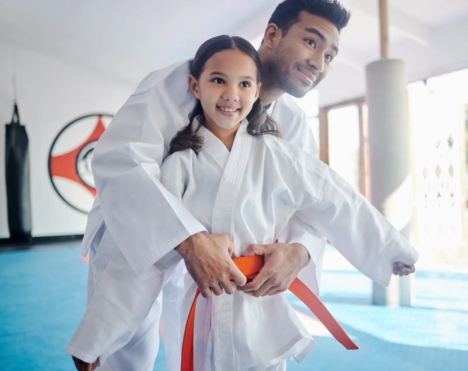 Instructor kneeling at mat level to adjust a young student's karate stance during a kids class