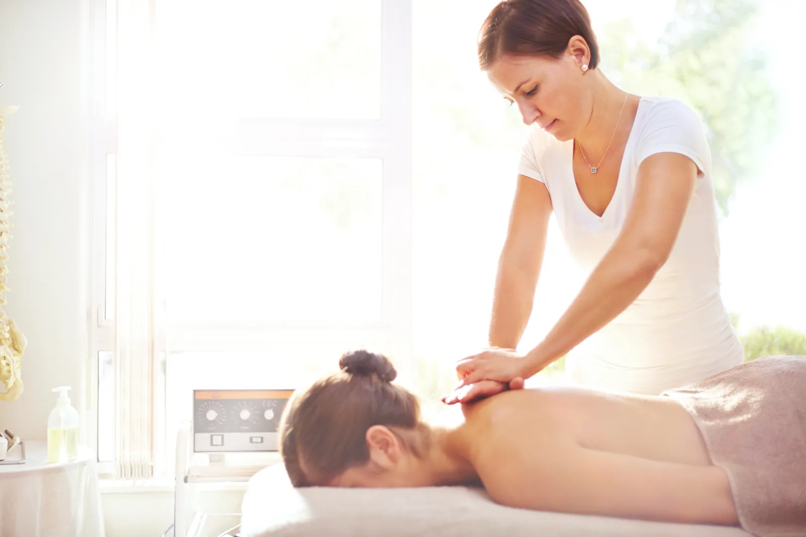 Massage therapist easing a client's shoulders in a softly lit day spa treatment room