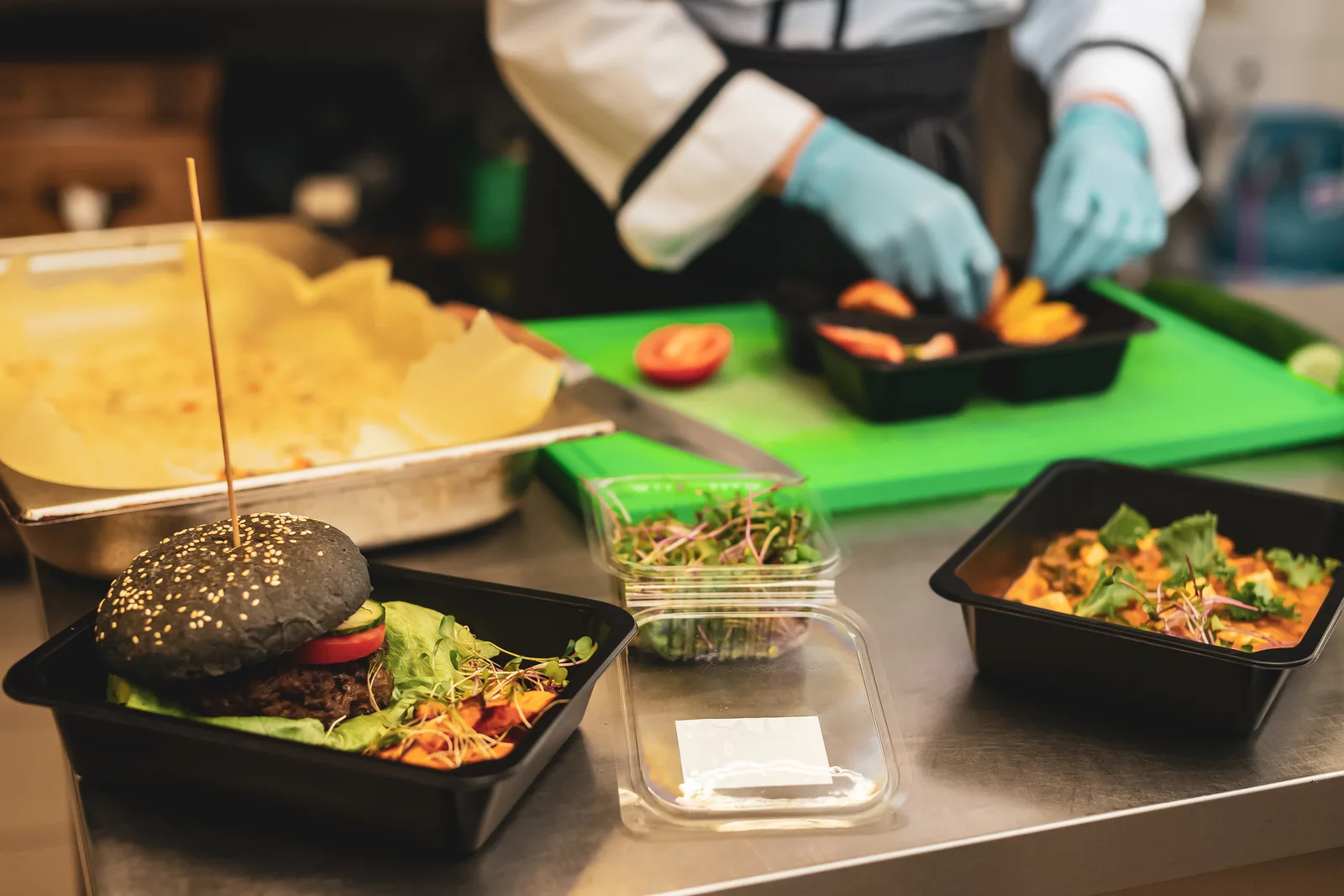 Meal prep cook portioning fresh cooked meals into rows of takeout containers in a commercial kitchen