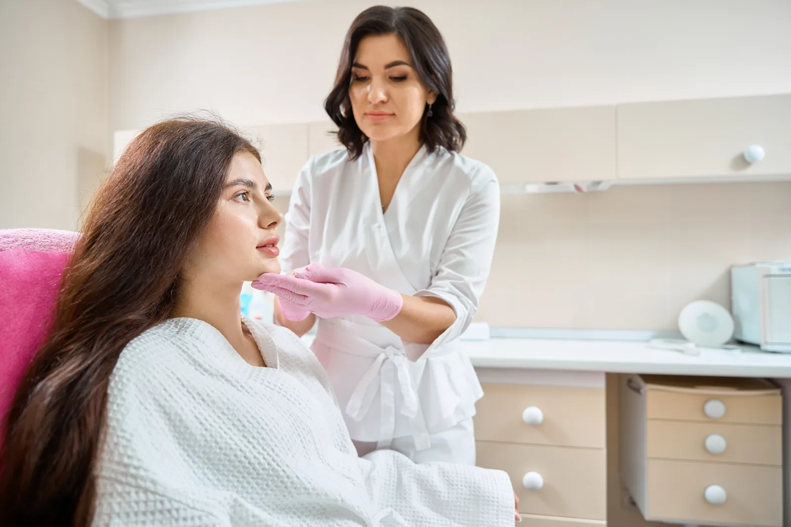 Nurse injector performing a facial treatment on a reclined client in a med spa treatment room