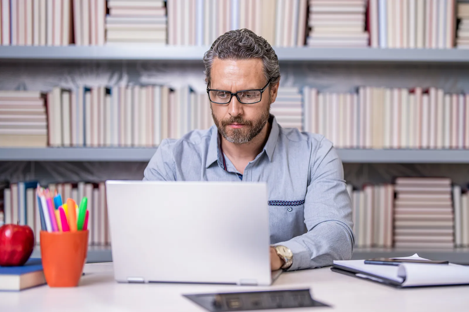 Membership site owner updating the content library and checking subscriber renewals on a laptop at a home office desk